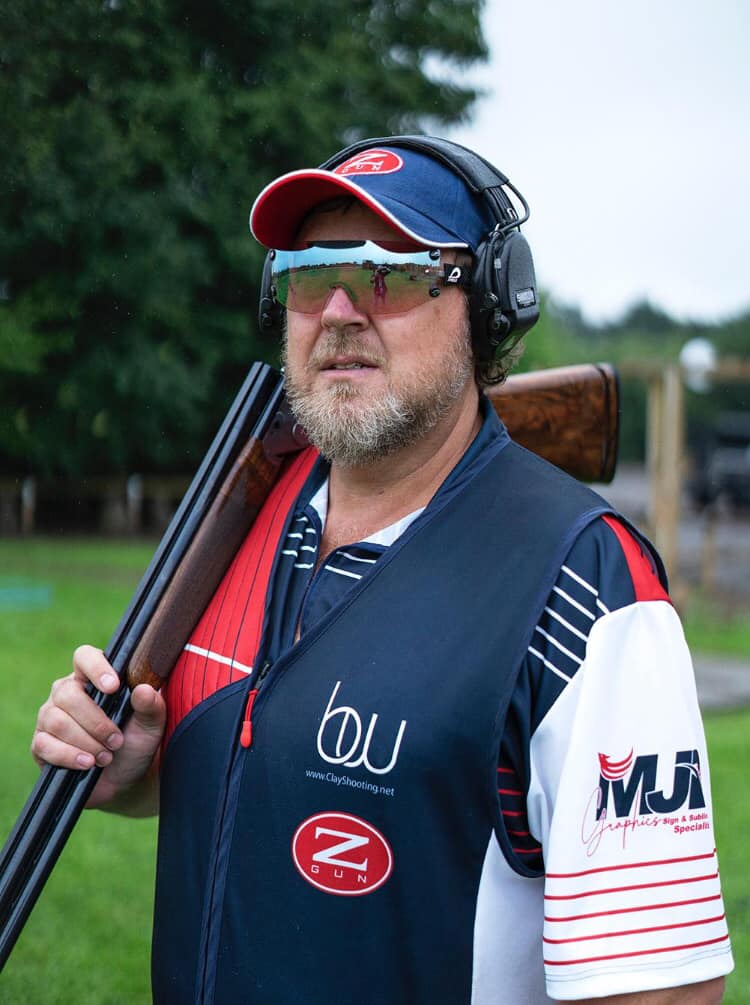 BW Clay Shooting coach Brent Woodard is stood in the Staffordshire countryside, holding his shotgun over his right shoulder.