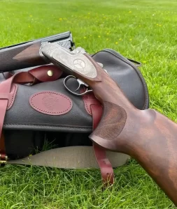 A fine-finshed shotgun lying on a Roar Leather bag with a stunning wallnut custom gun stock.